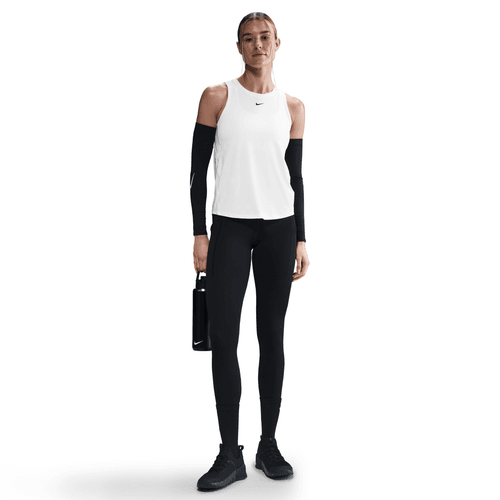 En person står på en hvid baggrund iført en Nike Dri-FIT Classic Tank Top, Dame, i hvid/sort, sammen med sorte leggings, sorte ærmer, sorte sportssko og med en sort vandflaske i højre hånd.