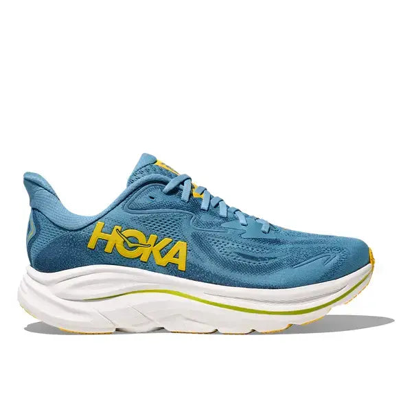 Hoka Clifton 10 til mænd i Alpine Blue/Foggy Night har en hvid polstret sål, gule detaljer og et fedt logo på siden, som ses i sideprofilen mod en hvid baggrund.