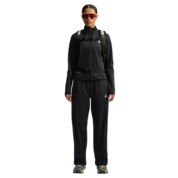En person iført en sort Nike Therma-FIT-trøje med 1/2-lynlås, sorte bukser, en rygsæk og orangefarvede solbriller.