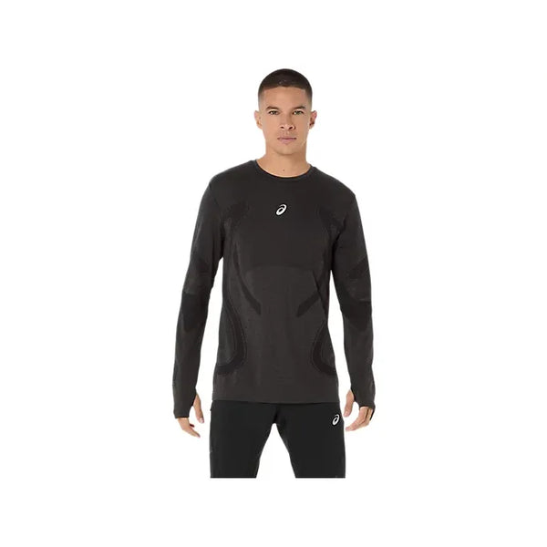 En person står med ansigtet fremad i Asics Road Seamless Ls Top, Herre, Performance Black - en langærmet sportstrøje med sømløs strikkonstruktion og et lille hvidt brystlogo - plus matchende sorte bukser på en almindelig hvid baggrund.