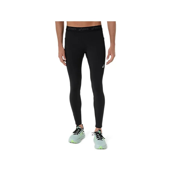 En person iført Asics Road Tight, Herre, Performance Black løbetights og lysegrå sko med grønne såler står på en almindelig hvid baggrund. Billedet viser ikke personens ansigt.