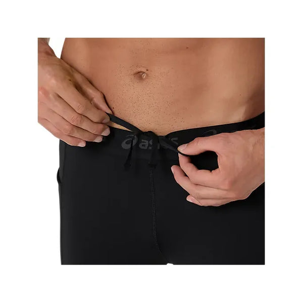 Nærbillede af en mand iført Asics Road Tight, Herre, Performance Black af hurtigtørrende strækstof, der binder snoren i linningen. Kun hans hænder og nedre del af maven er synlige.