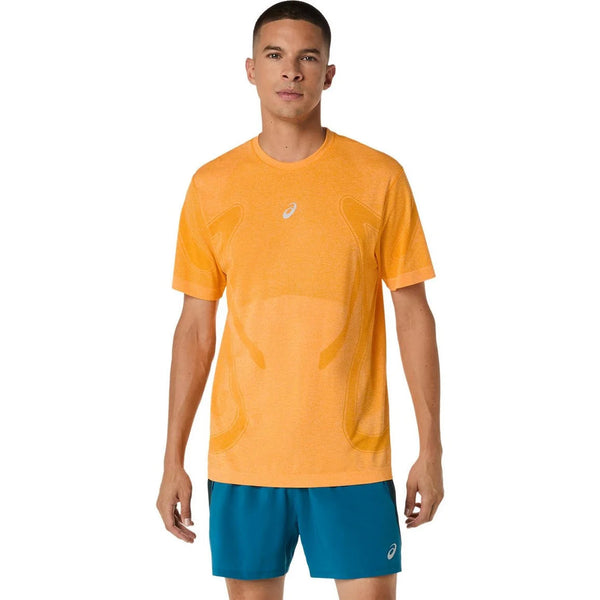 En mand kigger fremad iført Asics Road Seamless Ss Top, Herre, Yamabuki - en orange sportstrøje med et hvidt logo - og blå sportsshorts på en hvid baggrund.