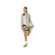 En person iført lysegrå jakke, Asics Fujitrail 2-N-1 Shorts til kvinder i Pepper/Performance Black, neongule sokker og neongule sneakers står på det ene ben og strækker det andet ved at holde anklen bag sig.
