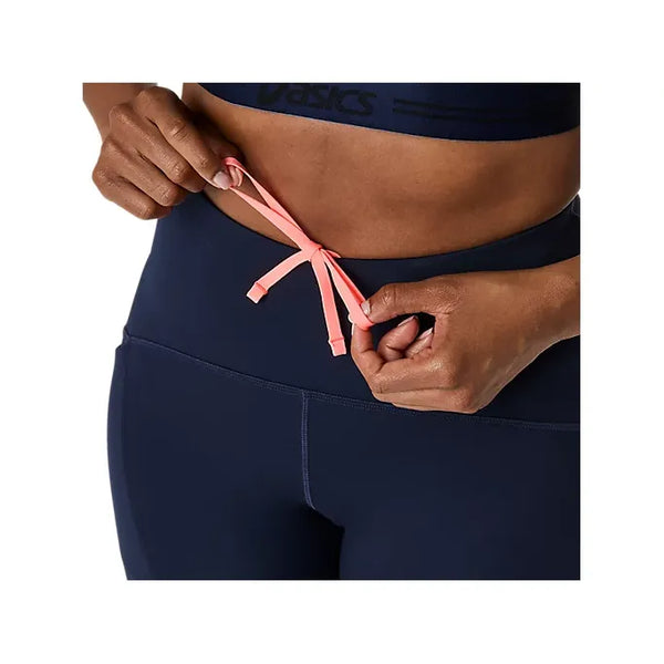 En person strammer den lyserøde løbegang på Asics Road High Waist Tight, Dame, Midnight, hvor kun midtpartiet og hænderne er vist.