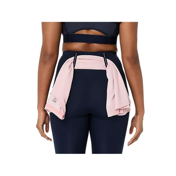En kvinde iført Asics Road High Waist Tight, Dame, i Midnight står med en lyserød sweatshirt bundet i taljen, set bagfra mod en hvid baggrund.