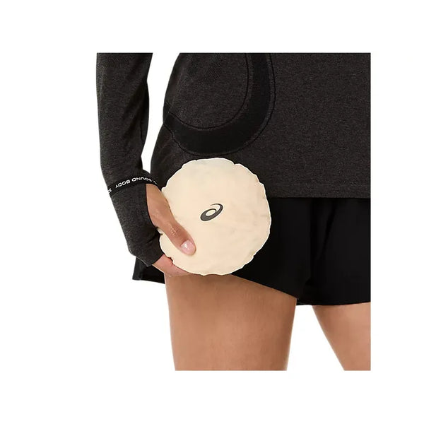 En person i sorte shorts og en langærmet top holder en beige rund genstand med Asics-logoet - ideel sammen med Asics Metarun Packable Gilet Dame Cream, en stilfuld løbevest til enhver løbetur.