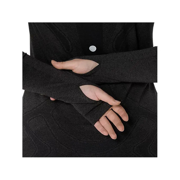 En kvinde bærer Asics Road Seamless LS Top i Performance Black/Graphite Grey, en langærmet trøje i genbrugsmateriale med huller til tommelfingrene, mens hun krydser sine hænder og underarme mod en almindelig baggrund.