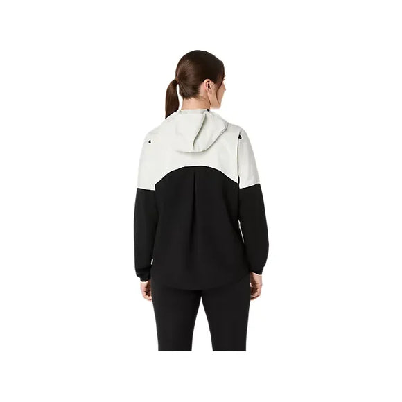 En kvinde med brunt hår i hestehale ses bagfra iført en Asics Metarun Legend Jacket til kvinder i Performance Black/Cream med et color-block design og sorte bukser.