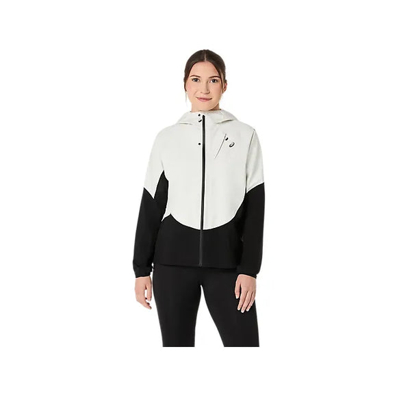 En kvinde med mørkt hår, der er trukket tilbage, kigger fremad iført ASICS Metarun Legend Jacket til kvinder i Performance Black/Cream, en sort og hvid løbejakke med lynlås og lange ærmer, kombineret med sorte bukser.