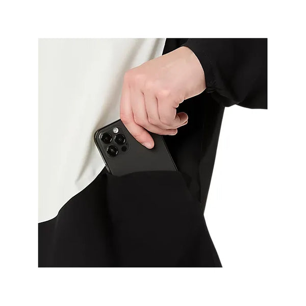 En persons hånd placerer en sort smartphone med flere kameraer på bagsiden i sidelommen på en Asics Metarun Legend Jacket til kvinder i Performance Black/Cream.