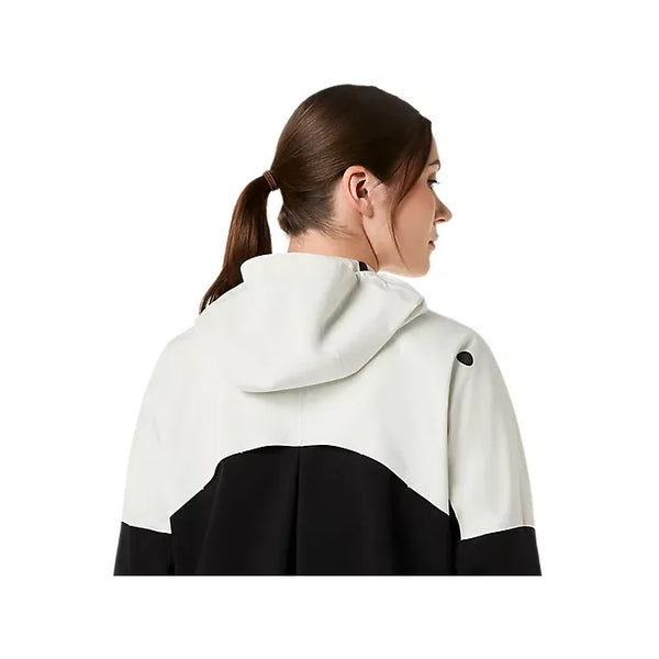 En kvinde med brunt hår i hestehale ses bagfra iført Asics Metarun Legend Jacket til kvinder i Performance Black/Cream. Jakkens hætte er oppe, men ikke over hendes hoved, på en almindelig hvid baggrund.