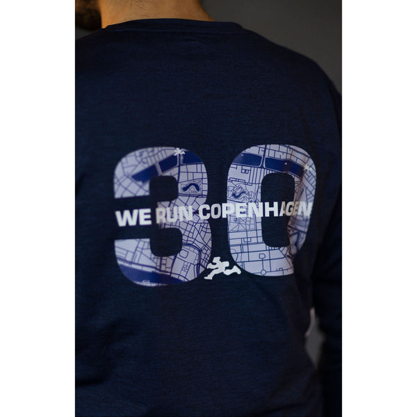 Nogen bærer den blå Saysky Marathon Sport 30 Års Jubilæum Clean Pace Long Sleeve med et stort "30" og et kort på ryggen med teksten "WE RUN COPENHAGEN", der fejrer hvert eneste løb i København.
