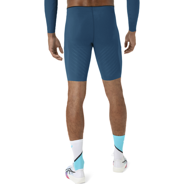 Der ses en person set bagfra, iført en blå langærmet cykeltrøje, Asics Metaspeed Tights Herre i farven Rich Navy, hvide og lyseblå strømper samt hvide cykelsko, foran en ensfarvet hvid baggrund.