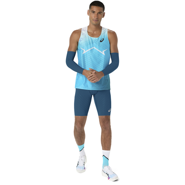 En mand står med ansigtet vendt fremad iført en blå og hvid sports-tanktop, Asics Metaspeed Tights Herre Rich Navy, blå armvarmere, hvide sokker og løbesko. Han holder sin venstre håndled med højre hånd.