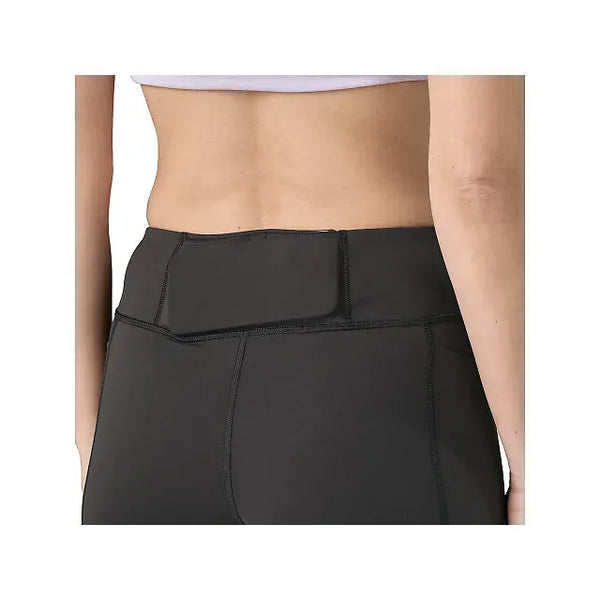 Et nærbillede viser en person fra taljen og ned iført Patagonia Endless Run Shorts 6in, Dame, Black med en lynlåslomme bagpå. Toppen af en lavendelfarvet sports-bh er også synlig.