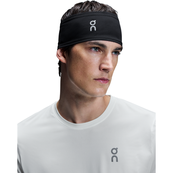 En person i hvid skjorte og et On Core Headband, Unisex, Black - begge med et minimalistisk logo - kigger lidt til siden mod en almindelig hvid baggrund.