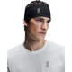En person i hvid skjorte og et On Core Headband, Unisex, Black - begge med et minimalistisk logo - kigger lidt til siden mod en almindelig hvid baggrund.