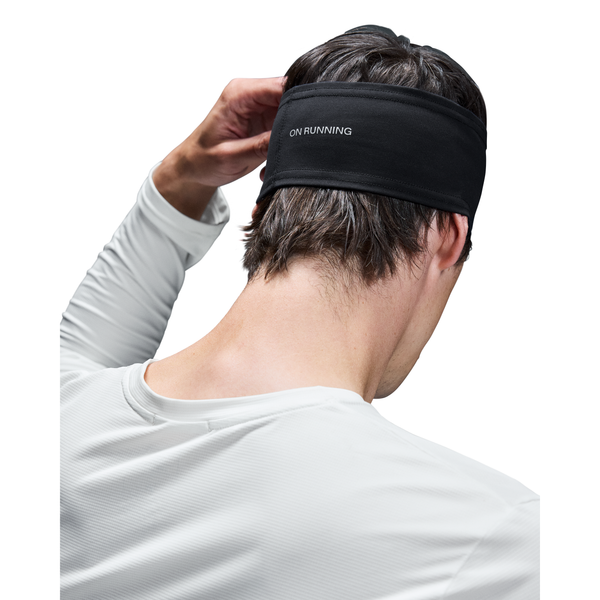 En person i en hvid langærmet skjorte med det sorte On Core Headband, set bagfra med en hånd på hovedet. Perfekt til løb.