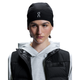 En person bærer On Core Beanie, Unisex, Black med hvidt logo, sammen med en lysegrå hættetrøje og en sort puffervest, og kigger lidt til siden mod en almindelig hvid baggrund.