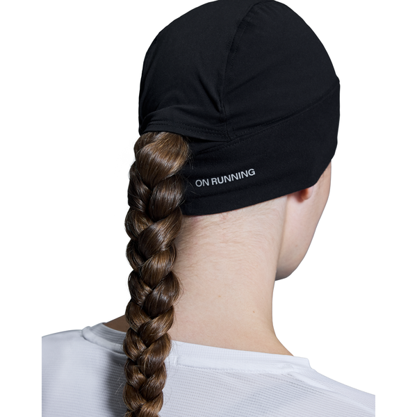 En person med en lang brun fletning, der er trukket gennem ryggen på en sort On-kasket, set bagfra, bærer en hvid top - ideel til at kombinere med On Core Beanie, Unisex, Black på kølige dage.
