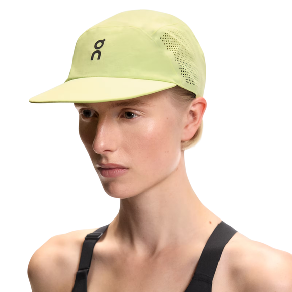 En person bærer On Performance Cap, Unisex, Lemonade - en lysegrøn kasket med perforering i siden og et sort logo - sammen med en sort sportstop og poserer på en hvid baggrund.