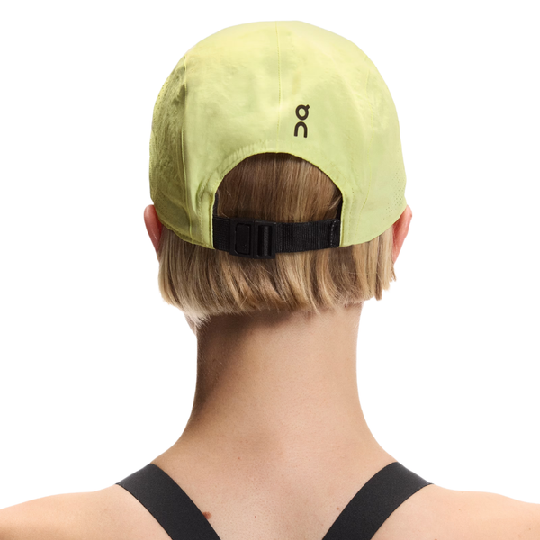 En person med kort, lysebrunt hår ses bagfra iført On Performance Cap, Unisex, Lemonade med sort, justerbar strop og et lille, sort logo. Personen er også klædt i en sort top med stropper.