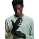 En person i en lysegrøn langærmet skjorte kigger ned, mens han justerer et par sorte Core Glove, Unisex-handsker fra On med et hvidt logo på en hvid baggrund.
