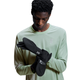 En mand i en lysegrøn langærmet skjorte kigger ned, mens han tager et par On Core Glove, Unisex, Black på med det hvide On-logo på håndleddet. Baggrunden er almindelig hvid.