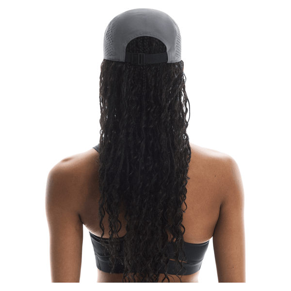 En person med langt, krøllet hår ses bagfra iført On Lightweight Cap, Unisex, Rock og en sort sports-bh på en hvid baggrund.
