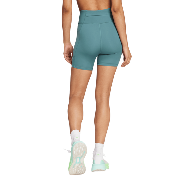 En person ses bagfra på en hvid baggrund iført Adidas OTR Short Tights 6", Dame, PRETEA, sammen med hvide sokker og lyseblå sneakers.