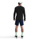 En person står med ansigtet vendt mod en hvid baggrund iført en Nike Dri-FIT ADV Wool langærmet løbetop til mænd i sort/antrazit, hvid kasket, mørkeblå shorts, lysegrønne sokker og sorte sportssko.
