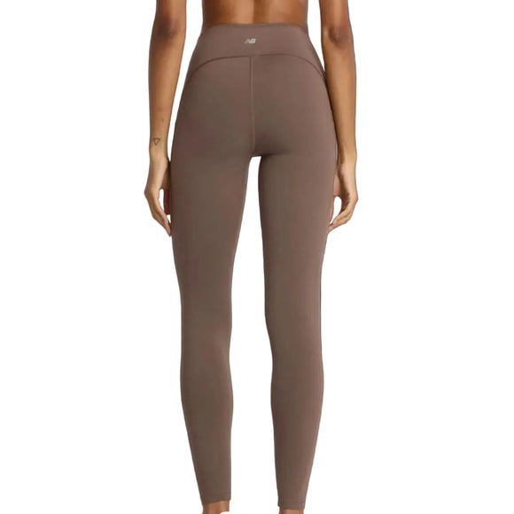En kvinde ses bagfra iført New Balance Sleek Pocket High Rise Legging 27, Dame, Cortado-højtaljede brune leggings med et lille logo i linningen, perfekt til træningstøj kvinder, på en ensfarvet hvid baggrund.
