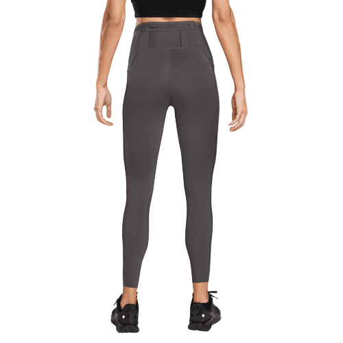 En kvinde kigger væk fra kameraet iført Nike Trail 7/8 Tights, Dame, i Thunder Grey/Black med en sort crop top og sorte sportssko, alt sammen på en almindelig hvid baggrund.