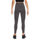 En kvinde kigger væk fra kameraet iført Nike Trail 7/8 Tights, Dame, i Thunder Grey/Black med en sort crop top og sorte sportssko, alt sammen på en almindelig hvid baggrund.