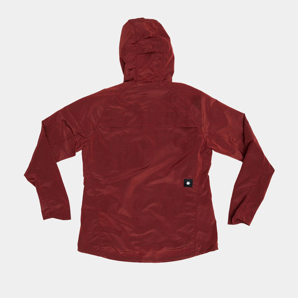 En rød W Clean Pace Shield Jacket fra Saysky til damer er lagt fladt på en hvid baggrund, vist fra ryggen. Jakken har lange ærmer og et lille sort rektangulært Saysky-mærke med en hvid stjerne nær nederste kant.