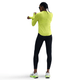En kvinde i en knaldgul Nike Dri-FIT UV Long-Sleeve Crew-Neck Running Top (Cyber/Htr/Reflective Silv), sorte leggings, hvide sneakers og solbriller står og strækker sin venstre arm ud over kroppen mod en almindelig hvid baggrund.