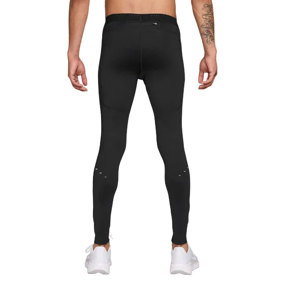 En mand vender sig væk fra kameraet iført Nike Stride Running Tight, Herre, Black/Reflective Silv og hvide sneakers. Han har bar overkrop og viser en tatovering på sin venstre arm mod en almindelig hvid baggrund.