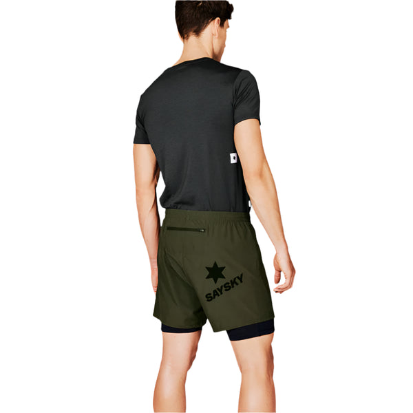 En mand står med ryggen til og er iført en mørk kortærmet skjorte og olivengrønne Saysky 2 in 1 Pace Shorts 5'' til mænd med en sort stjerne og SAYSKY-logoet bagpå på en almindelig hvid baggrund.