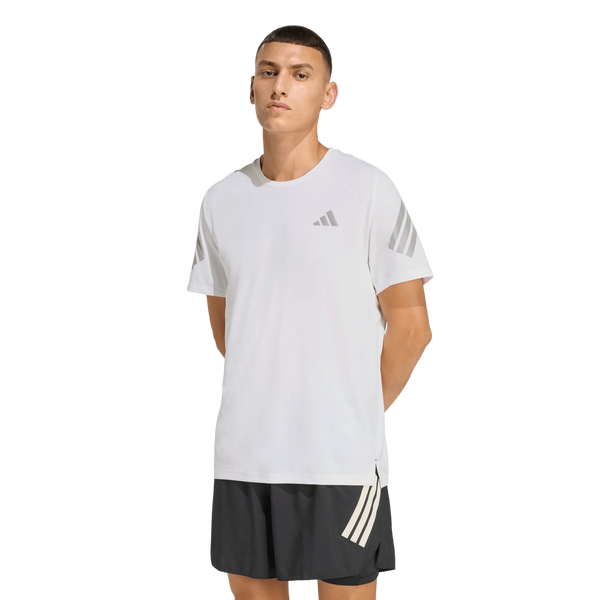 En person står på en hvid baggrund iført Adidas Adi365 Running Tee, Herre, White med grå ærmestriber og et lille logo på brystet, sammen med sorte shorts med hvide striber på venstre ben.
