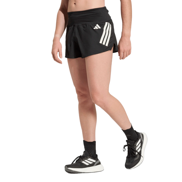 En person i Adidas Adi365 Shorts, Dame, Black står på en almindelig hvid baggrund. Kun den nederste halvdel er synlig, med sorte shorts med hvide striber, sorte sokker og sorte Adidas-løbesko.