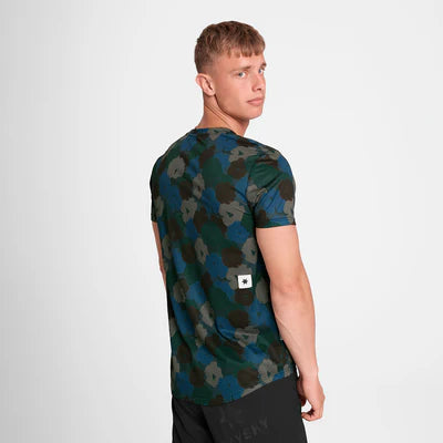 En mand med kort lysebrunt hår kigger sig over skulderen iført Saysky Flower Combat T-Shirt, Herre, Blue Aop med et lille hvidt mærke nederst på ryggen og sorte shorts. Baggrunden er helt hvid.