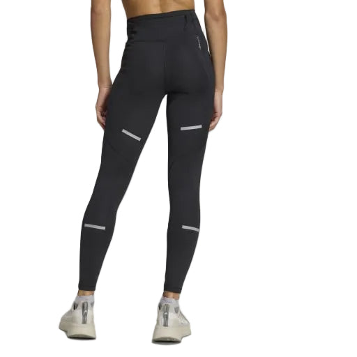 En person kigger væk og er iført Adidas Adi365 Leggins, Dame, Black med refleksstriber og grå sportssko på en almindelig lysegrå baggrund.