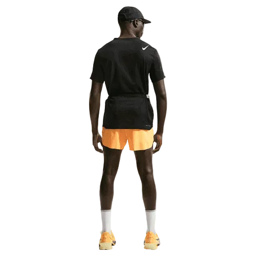 En mand står med ryggen til og er iført sort kasket og t-shirt, Nike AeroSwift 4In Brief-Lined Running Shorts i Laser Orange/Black, hvide sokker, orange sneakers og en sort bæltetaske på en almindelig hvid baggrund.