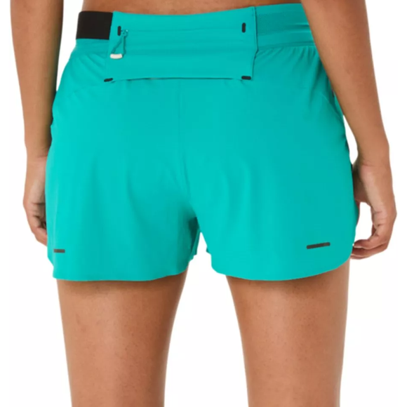 En person ses fra taljen og ned iført Asics Metarun Split Short, Dame, i Wave Teal, med en baglomme med lynlås. Hænderne er afslappet langs siden.
