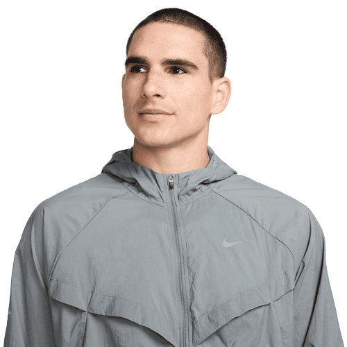 En mand med kort mørkt hår er iført Nike Repel UV Running Jacket, Herre, i Smoke Grey/Reflective Silv, med UV-beskyttelse og hætte. Han kigger lidt til siden mod en almindelig hvid baggrund.