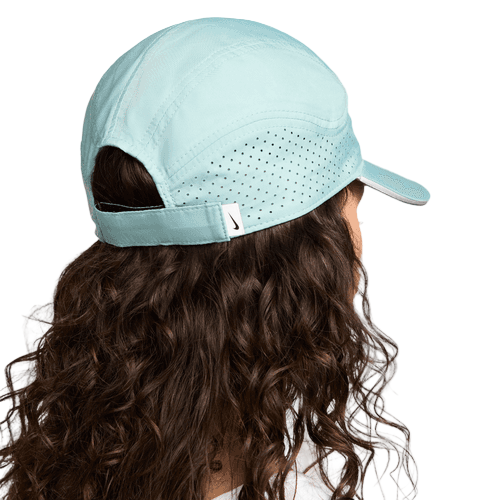 En person med langt, krøllet brunt hår ses bagfra iført Nike Adv Fly Cap Unisex i Cannon/Anthracite/Reflective Silv med perforeret bagpanel, Dri-FIT-teknologi og en justerbar strop, der giver god komfort.