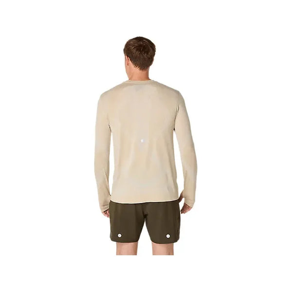 En person står og kigger væk fra kameraet iført en cremefarvet Asics Road Seamless LS Top til mænd og mørkegrønne shorts på en almindelig hvid baggrund.