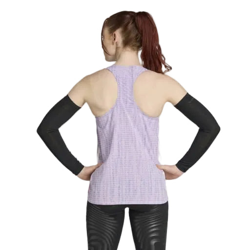 En kvinde med langt, rødligt hår i hestehale står med hænderne på hofterne mod en hvid baggrund iført en Adidas Adizero Singlet Dame i Powplu/Maglil, sorte ærmer og skinnende sorte leggings - klar til løb.
