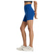 En kvinde bærer en sort crop top og New Balance Sleek Pocket High Rise Short 6" i Galaxy Blue, lavet af fugttransporterende stof med sidelommer, sammen med hvide sneakers. Fra siden ses hendes overkrop og ben mod en hvid baggrund.